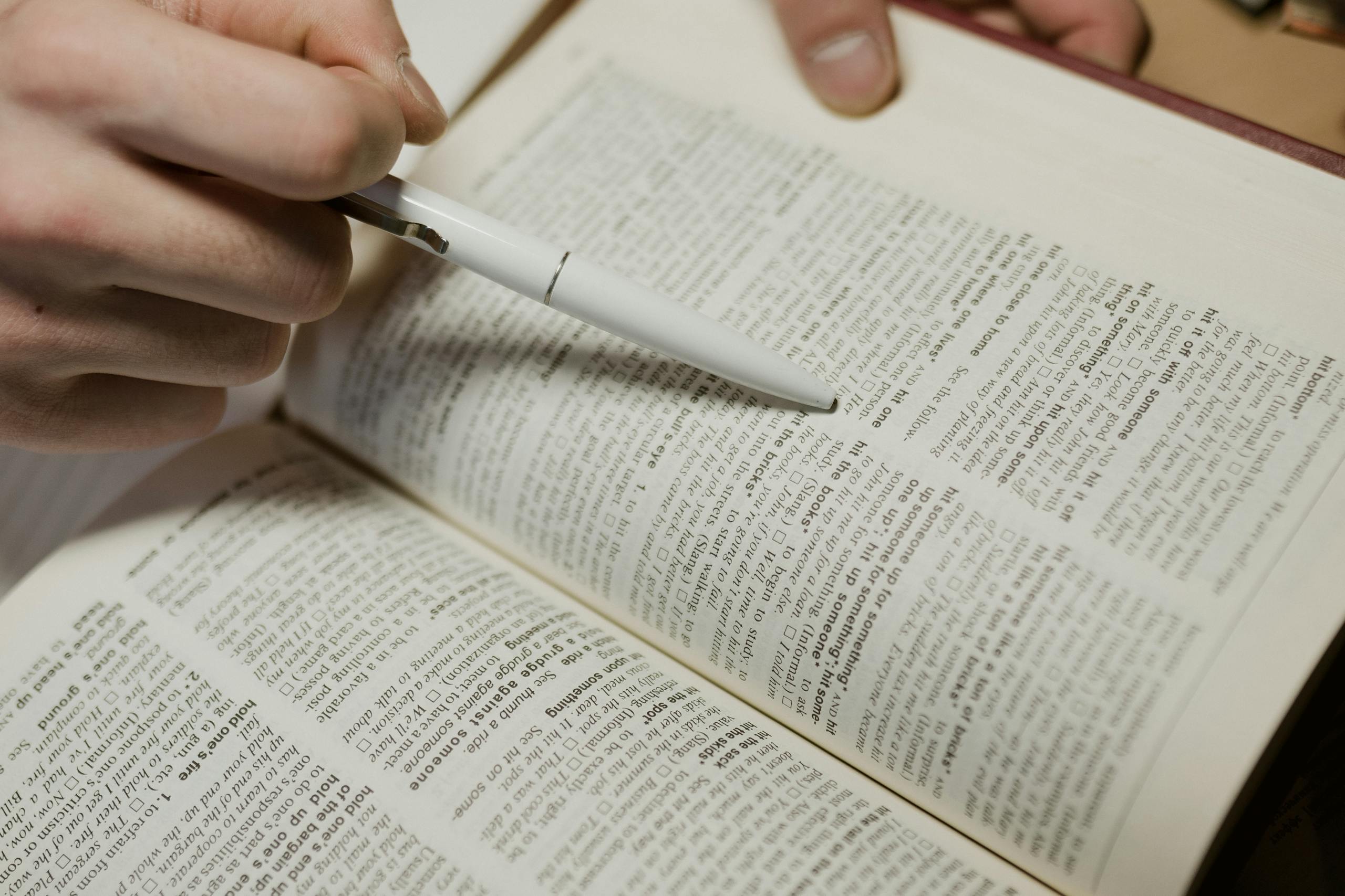 A close-up image of a hand using a pen to point at text in a book.
